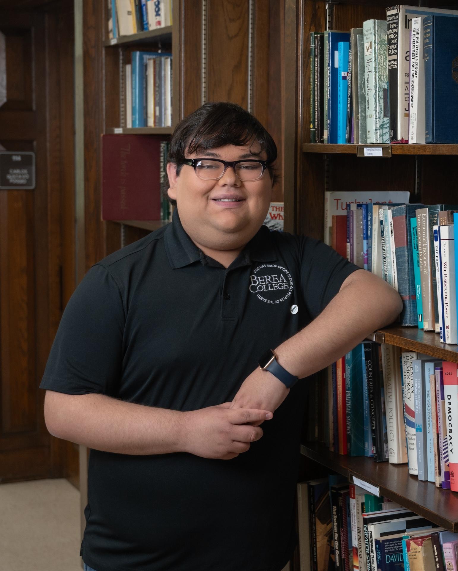 Berea student, Abraham '26, leaning against a bookshelf while smiling at the camera.